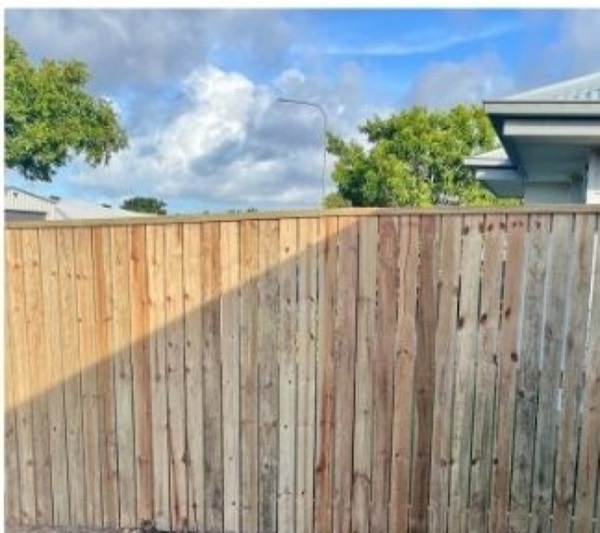 A timber paling fence with a house and trees behind it