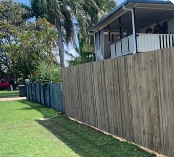 A timber paling fence beside a Queenslander home and palms