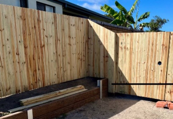 A timber fence and double gate with banana palms behind