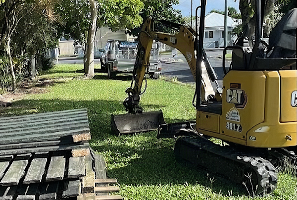 A mini excavator and stacked timber on a Mackay job site