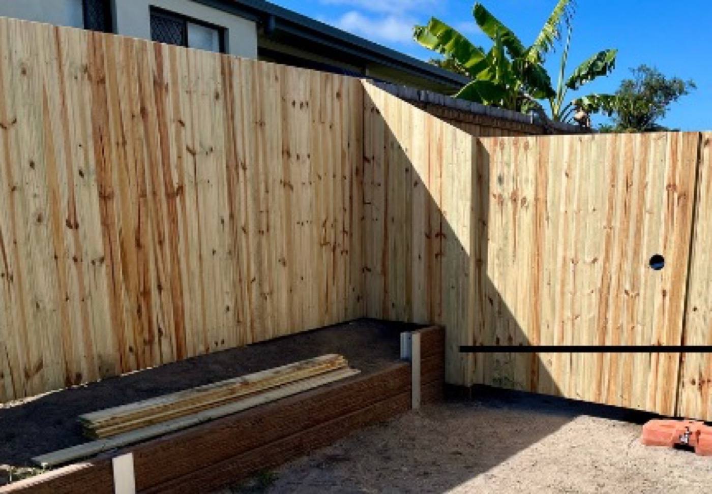 A timber double gate and fence with banana palms behind