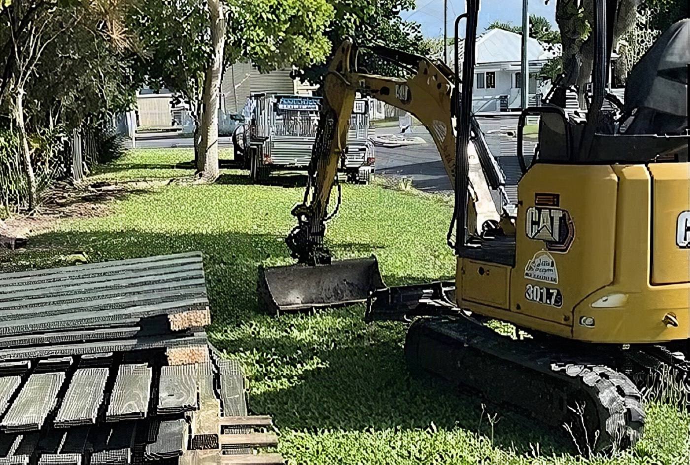 A mini excavator and stacked timber on a Mackay job site